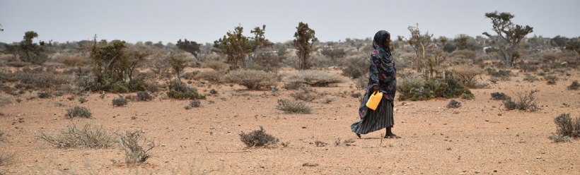 A woman in Somalia walking in the desert with a water bottle