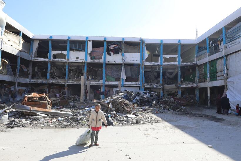 A child stands in front of a destroyed building.