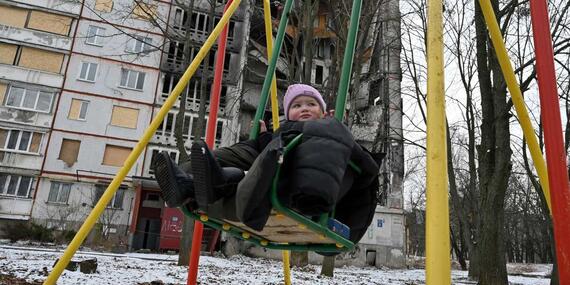 A child on a swing in front of an apartment block partially destroyed by shelling