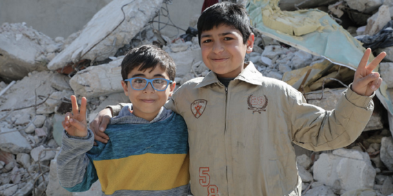 Two boys stand in front of the rubble of war in Syria
