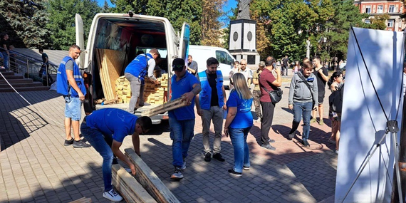 People unload wood planks from an open van.