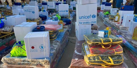 Cardboard boxes bearing UNICEF, WFP and other UN agency logos are stacked up with mattresses and blankets in rows of lots on the ground