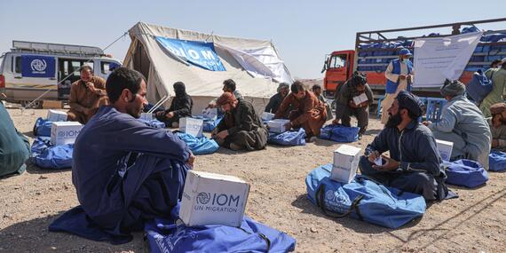 Men sit on the ground with stacks of aid.
