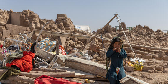 A little girl sits amid debris and rubble with a juice box.