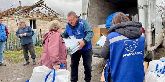 A man in a blue vest hands out a package from the back of a truck to a woman