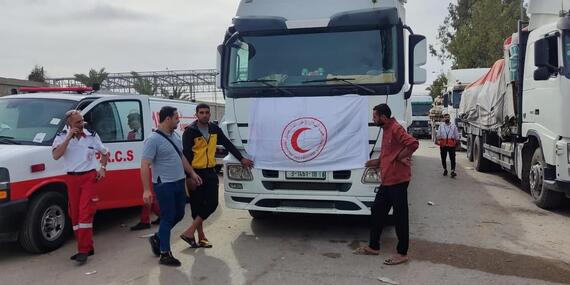 Loaded trucks, one of them with a Red Crescent are parked on a road.