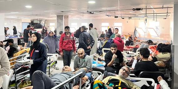 Inside of a hospital - people with bandages are lying on rows of hospital beds in a crammed space.