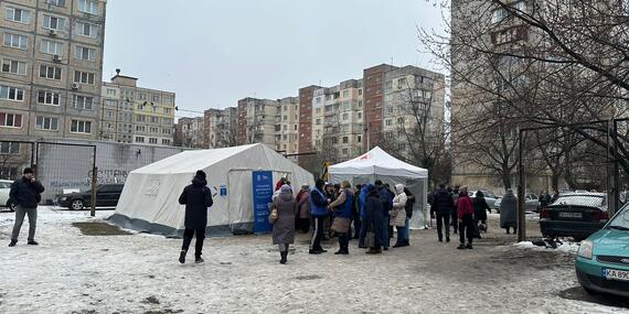 People gathered near two tents on a snow-covered open ground.