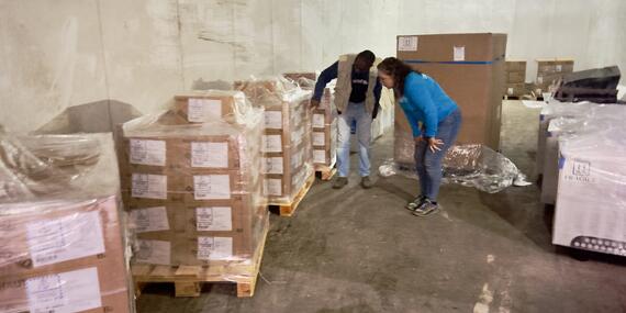 Two people - a man and a woman examine wooden sealed cartons piled in a room.
