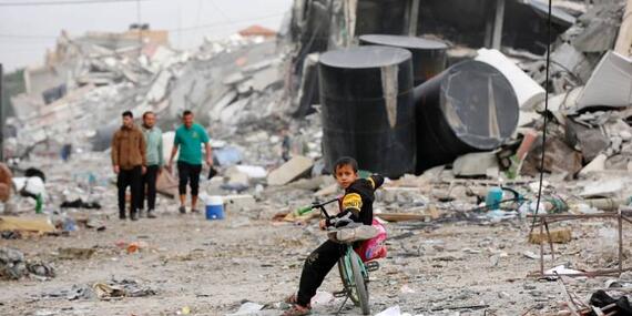 A young boy on a bike surrounded by the rubble of collapsed buildings in Gaza City.
