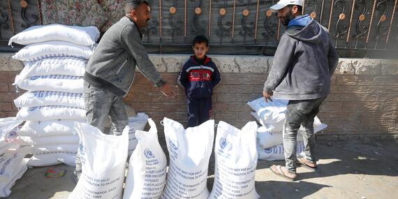 Two men and a young boy stand near a pie of sacks bearing a UN logo.