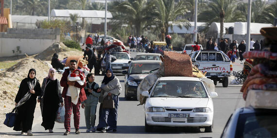 Women, men, children walk on a road with bags. Cars loaded with bags can also been in the photo