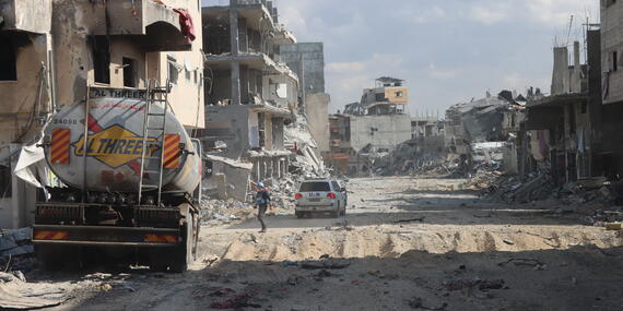 A UN vehicle is seen on a destroyed road with ruins of buildings and destruction all around.