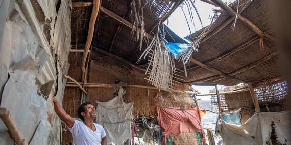 A man standing in an informal shelter in Ethiopia's Afar Region looks up at the gaping holes in the roof. 