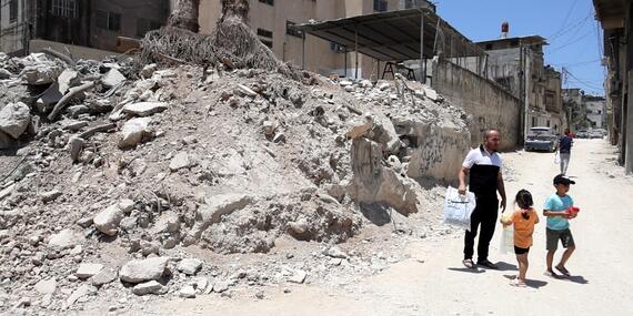A man walks with two children past rubble and destruction in an urban area of Tulkarm.