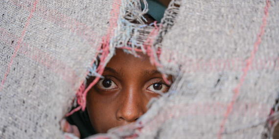 An internally displaced child looks out of a piece of cloth. She lives in Al Rebat IDPs Camp in Lahj, Yemen.