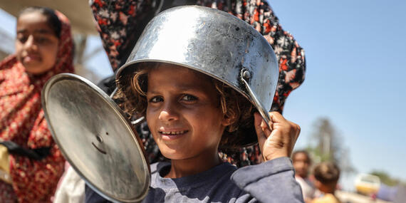 A young girl in Gaza wears a pot as a hat while waiting for food rations.