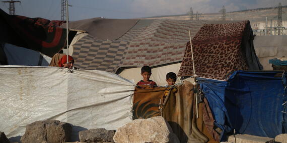 Children in a displacement camp stand amidst makeshift shelters in North-west Syria