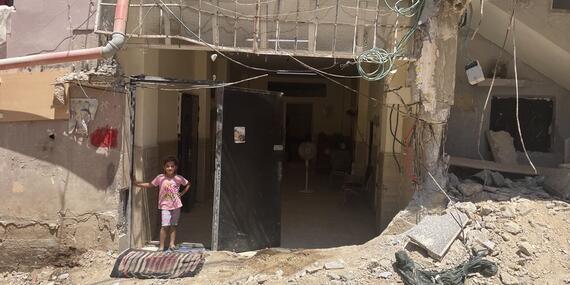 A girl stands in the doorway of a damaged building