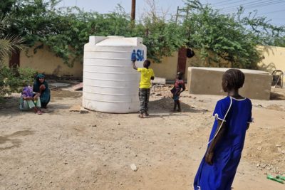 A child leans against a plastic water tank that stands on the ground.