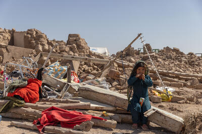A little girl sits amid debris and rubble with a juice box.