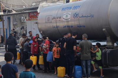 A water tanker with children and men lining up with buckets and containers.