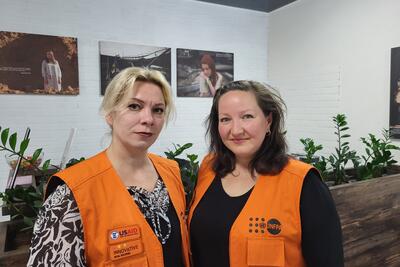 Two women in orange vests that read UNFPA and USAID smile at the camera.