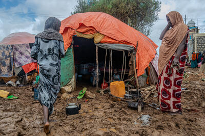Two women stand outside their flooded informal shelter in mud