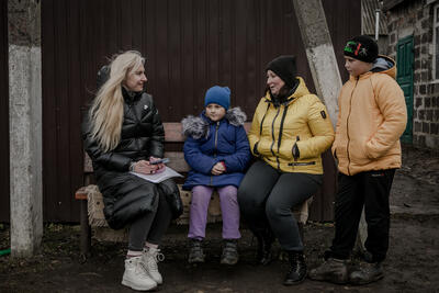 A woman talks to a woman and a young girl and boy outside a building.