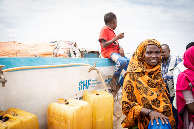 Women and a young boy stand near some jerry cans and a tap in Galkayo, Somalia.
