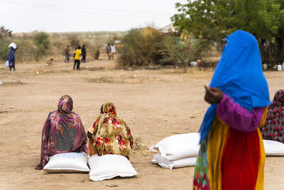 People sitting in an open field waiting for food distribution in Sudan.