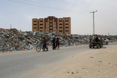 People walk past mounds of waste in Gaza. Photo: UNRWA.