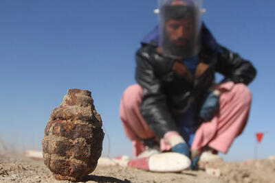 A man sits crouched on a ground with a protective mask in Kandahar Province. In front of him is an ordnance.