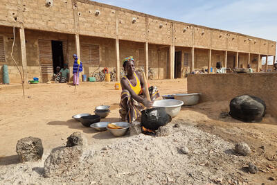 A displaced woman prepares millet in a school’s courtyard where she and her family have taken shelter. Burkina Faso.