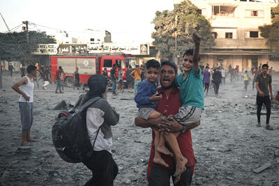 A father carries his children while trying to flee from air strikes in the city of Rafah. November 2023.