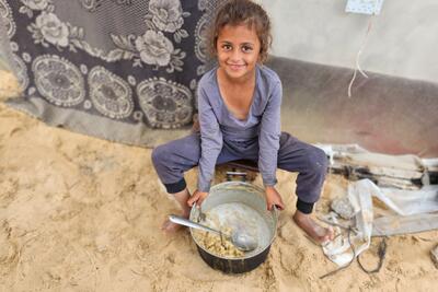 Mayar, 7, holds a pot of food in front of her family tent at the Al-Mawasi displacement camp, southern Gaza.