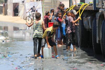 Children gather around a water truck to collect water amidst challenging conditions in Gaza.