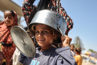  A young girl in Gaza wears a pot as a hat while waiting for food rations.
