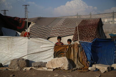 Children in a displacement camp stand amidst makeshift shelters in North-west Syria