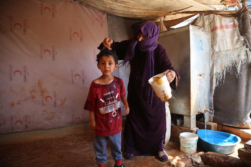 A woman pours water over a child to help him cope with the heat in Al-Hamra camp for internally displaced people in Syria’s Idleb governorate. Photo: OCHA/Bilal Al-Hammoud