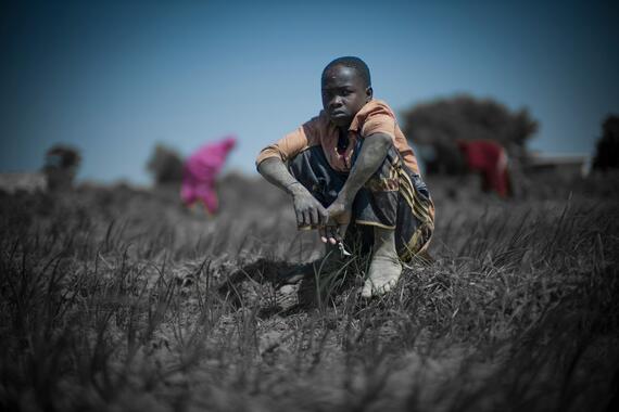 A boy sits face to camera helping his mother in the field