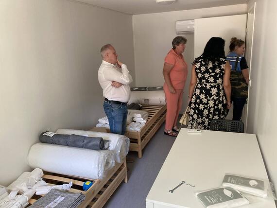 People stand in a room with three beds. 