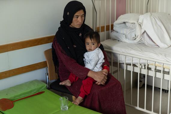 A woman with a baby on her lap sits near a hospital bed.