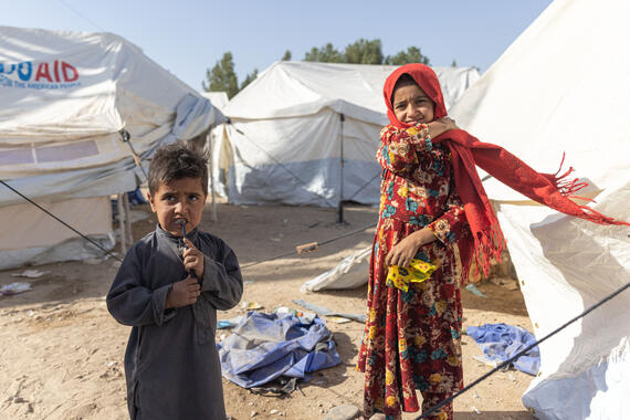 A boy and a girl stand outside tents on an open ground.