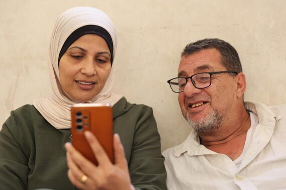A woman holds a mobile phone in her hand, a man seated next to her is also looking at the phone.