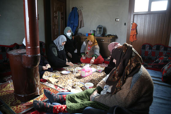 A group of women are seated on a carpeted floor. There are plates of food in front of them.