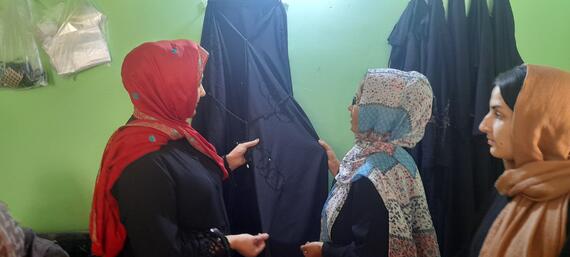 Women examine hijabs on a hanger in a room.