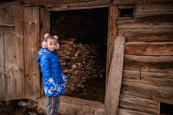 Oleksandra, 10, stands next to a pile of a firewood provided by aid workers to her family.