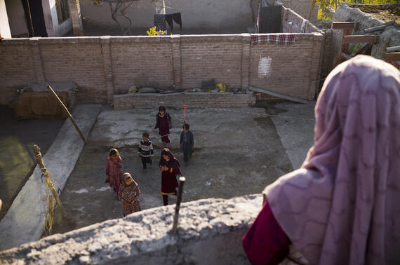 An Afghan woman standing over a balcony watching people walk in a compound.