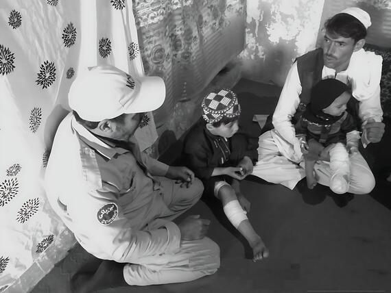 Two children with bandaged legs sit with two men. One of the men is holding one of the children in his lap in Afghanistan's Paktya Province.